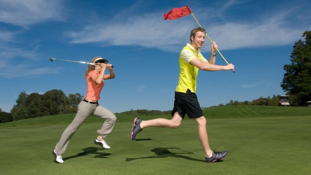 Corredor con la bandera de un hoyo de golf y golfista persiguiéndolo con el palo de golf