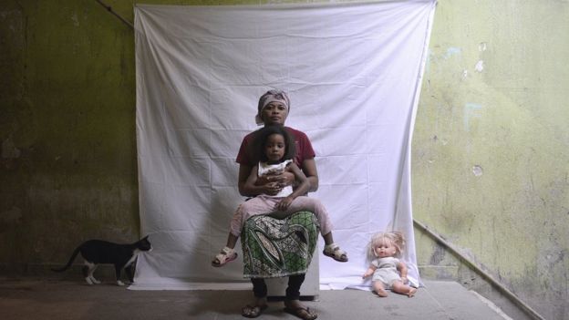 Retrato de mãe e filha congolesas que vivem em Ramos, na zona norte do Rio, ao lado do gato de estimação da família