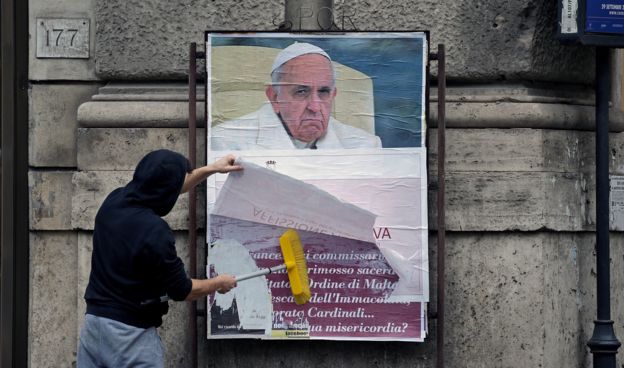 Un trabajador de la Alcaldía de Roma tapa uno de los carteles que cuestionan al Papa.