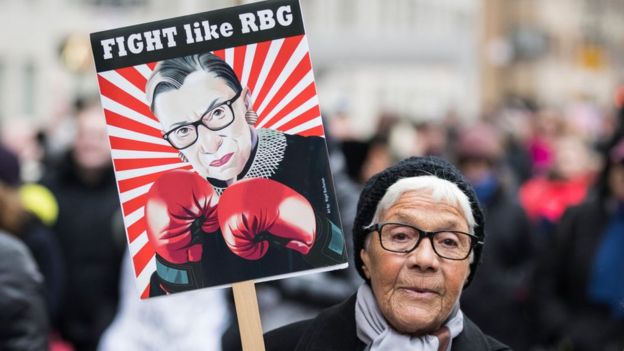 A woman brandishes a sign with Ruth Bader Ginsburg's likeness on it