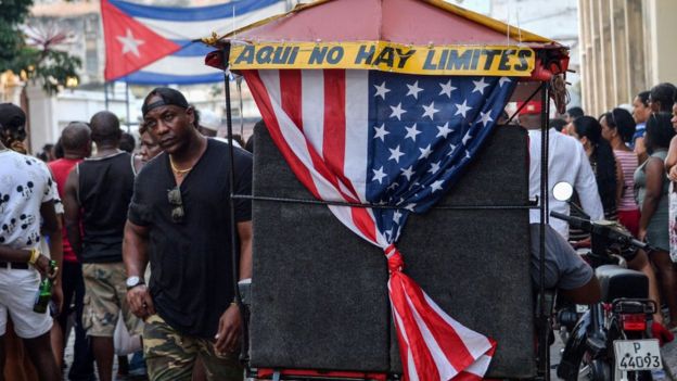Bandeira americana próxima à frase "Aqui não há limites", em uma rua cheia de gente em Cuba