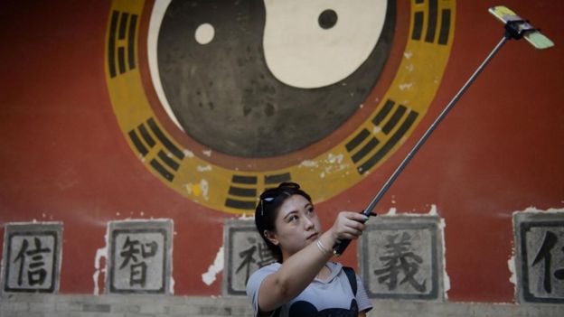 Una persona tomándose un selfie con un signo de yin y yang pintado en una pared
