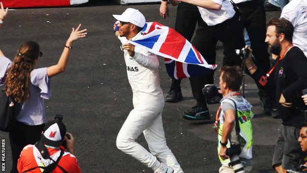 Lewis Hamilton runs among fans with a Union Flag draped over his shoulders