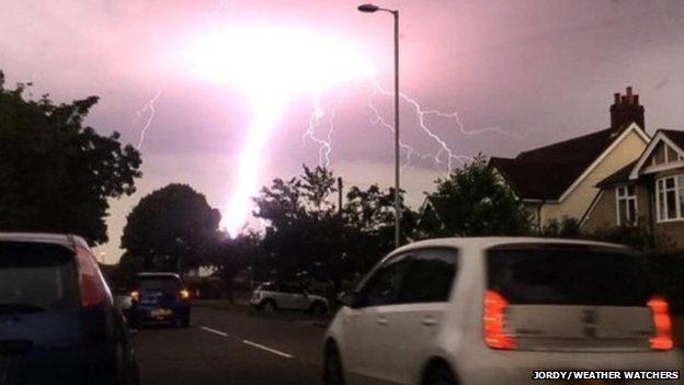 Huge bolt of lightning behind trees on a busy road