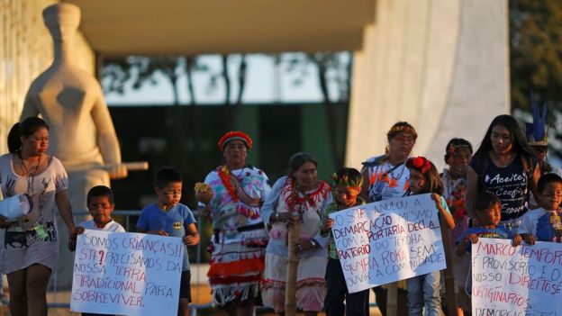Integrantes do povo Guarani Kaiowa seguram cartazes de protesto em frente a estátua que representa a Justiça em BrasÃlia