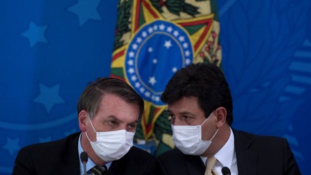 Bolsonaro e Mandetta aparecem de máscaras, falando próximos entre si, em evento