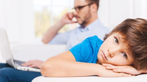 Niña mira a sus padres mientras utilizan sus teléfonos celulares.