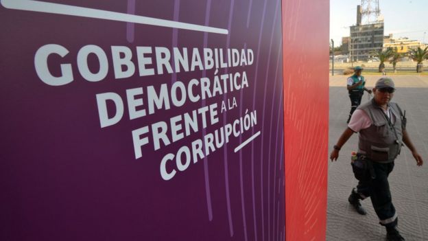 Un funcionario pasa frente al cartel de "Gobernabilidad democrática frente a la corrupción" para la Cumbre de las Américas en Lima, Perú.