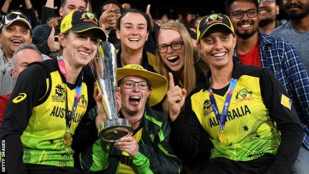 Gardner with the trophy, team-mates and supporters celebrating Australia's victorious 2020 T20 World Cup campaign
