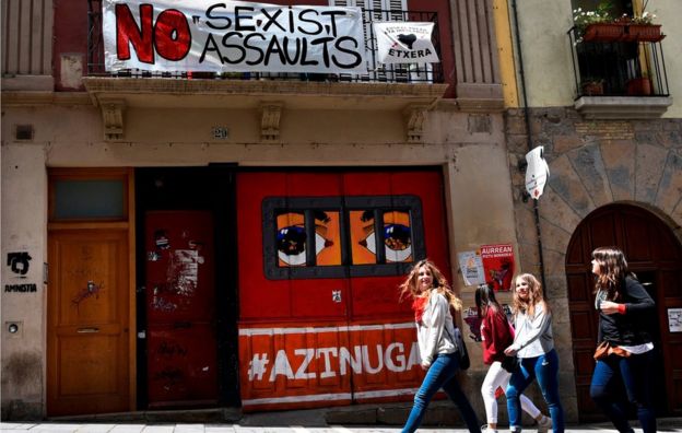 Revellers walking past a banner protesting against the growing number of sexual assaults during the San Fermin bull-run festival in Pamplona on 13 July 2016