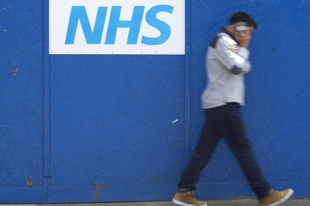 Man walking past NHS sign