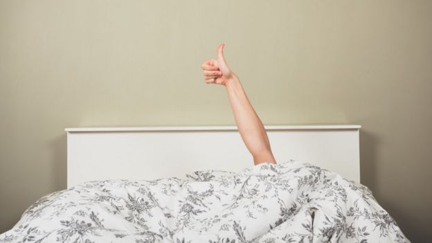 A young woman in a bed is giving thumbs up