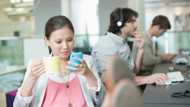 Mujer con una taza y mirando su celular