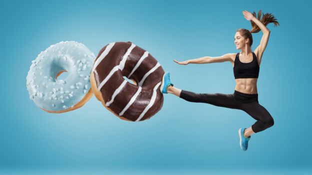 Mujer en forma pateando dos donuts gigantes.