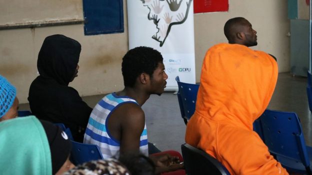 Haitianos sentados esperam por atendimento em dependências de órgão público
