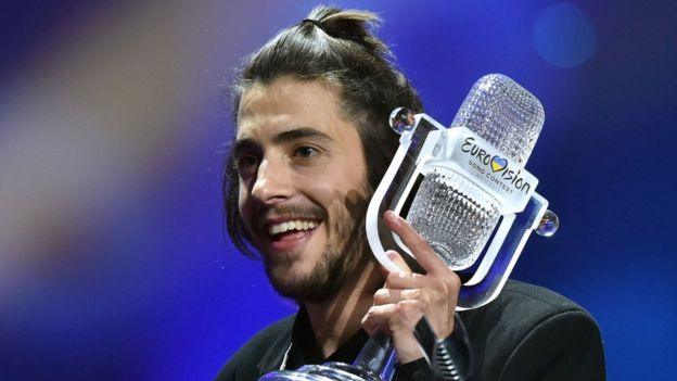 Salvador holds the glass microphone aloft as he greets the press after his victory