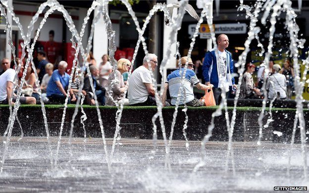 People enjoy the sunshine beside a pavement fountain in Liverpool on 30 June