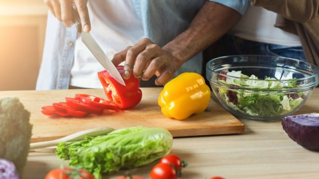 Man chopping a pepper surrounded by fresh produce