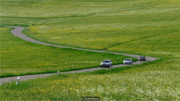 Carros circulam numa via sinuosa no sul da Alemanha, em meio a campos de canola