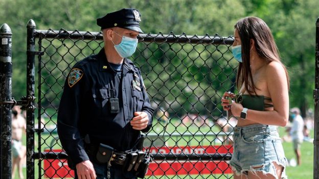 Полицейский в маске в Центральном парке Нью-Йорка разговаривает с девушкой в маске
