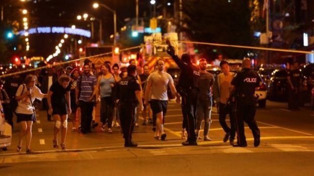 Foto tirada em 22 de julho de 2018 mostra policiais e pedestres cruzando área isolada pela polícia após o ataque a tiros em Toronto