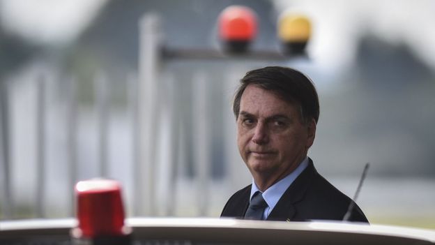 Bolsonaro em área externa, perto de carro, de onde se pode ver sinalizadores de viaturas