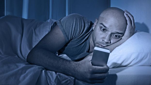 HOmbre viendo el celular en la cama.