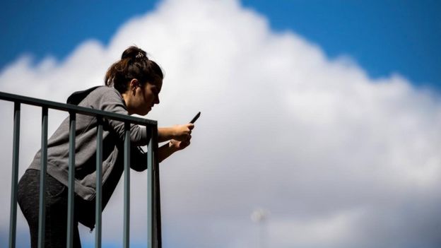 Mulher olha no celular em uma sacada