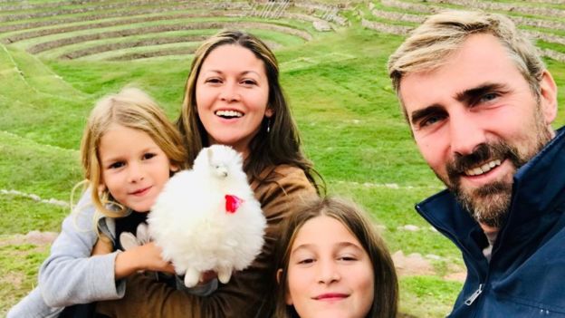 Pai, mãe e duas filhas posam em frente a uma ruína histórica no Peru