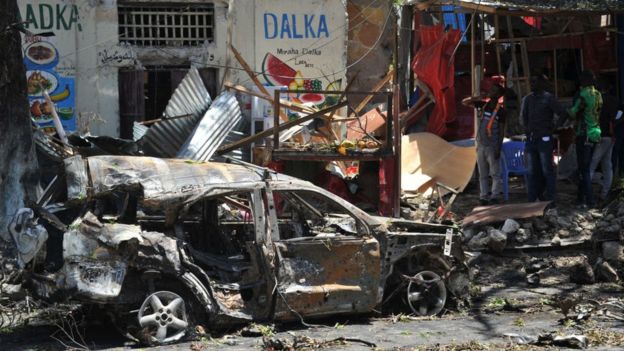 Los escombros de un auto destrozado por una bomba frente a tiendas de comercio en la capital somalí de Mogadiscio