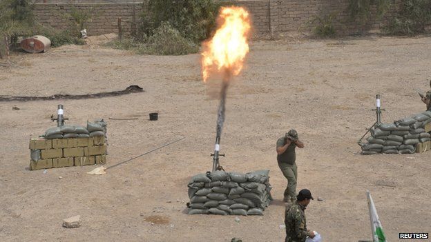 An Iraq Shiite paramilitary personnel launches a mortar round toward Islamic State militants on the outskirt of Bayji