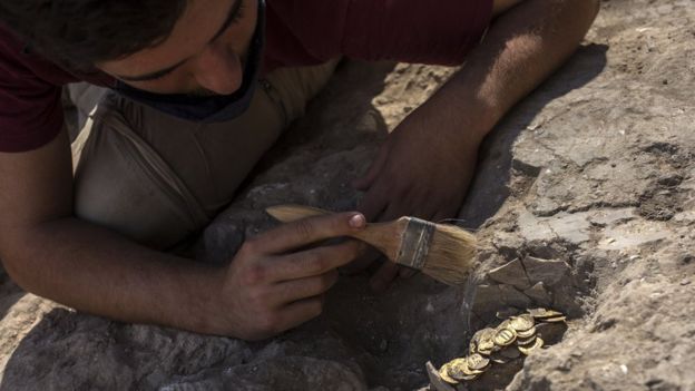 Volunteer Oz Cohen brushes away dust from gold coins found at an archaeological dig in central Israel (18 August 2020)