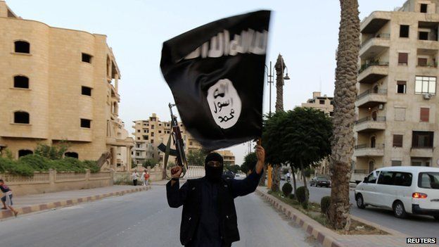 A lone armed and masked Islamic State militant waving an Isis flag on a deserted street in Raqqa, June 2014