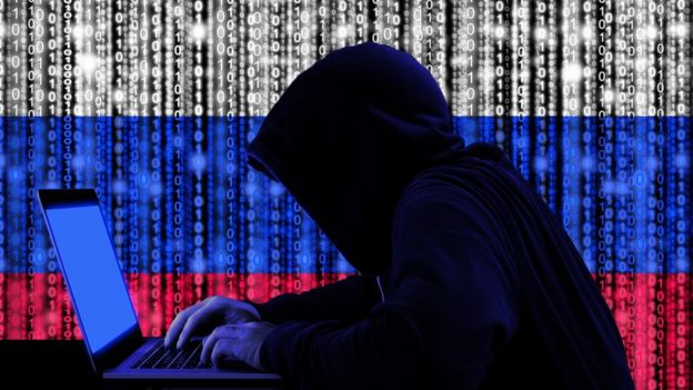 Encapuchado con computadora frente a una bandera rusa