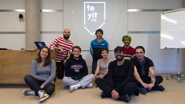Eight members of the Teyit team sit in their office in front of their logo, smiling together