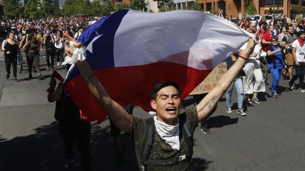 Joven con una bandera de Chile delante de cientos de manifestantes.