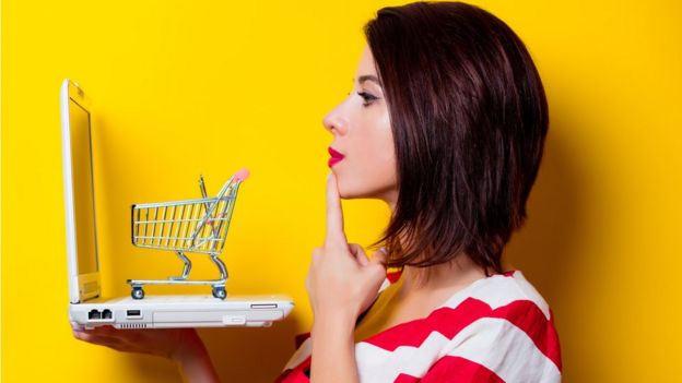 Una mujer con una computadora portátil y un carrito de compras.