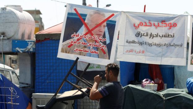 An Iraqi protester walks past a poster rejecting new Prime Minister Mustafa al-Kadhimi in Tahrir Square, Baghdad, Iraq (7 May 2020)