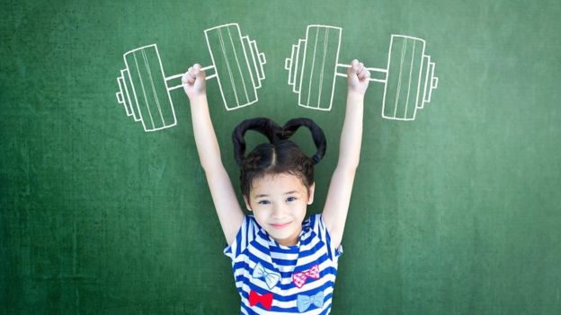 Niña contra un pizarrón en el que hay pesas dibujadas