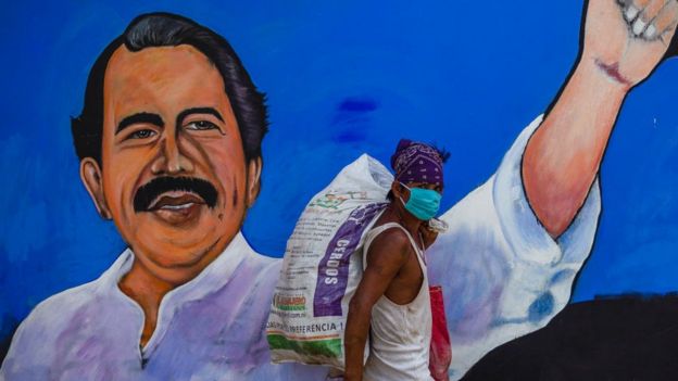 Hombre con máscara pasa frente a un mural con el rostro de Daniel Ortega.