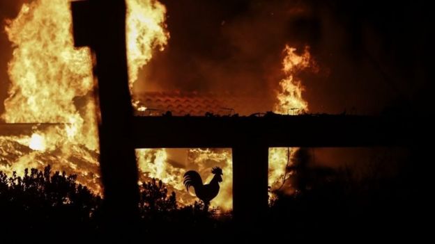A rooster decoration in a burning house is seen during a forest fire in Mati a northeast suburb of Athens, Greece, 23 July 2018
