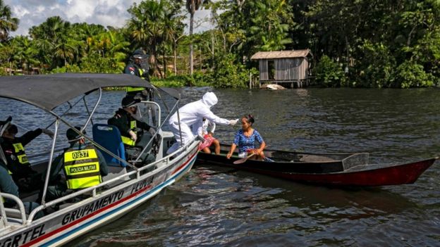 A partir de um barco, profissional todo coberto de jaleco examina mulher em outro barco de madeira, em rio da Amazônia
