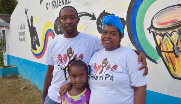 Gustavo Reyes poses in front of a mural with his wife and daughter