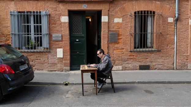 A man sits at a desk in the middle of a parking space