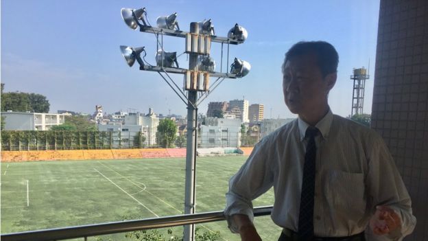El director de la escuela Kim Seng Fa, detrás el campo de deportes. (Foto: Francisco Jiménez de la Fuente)