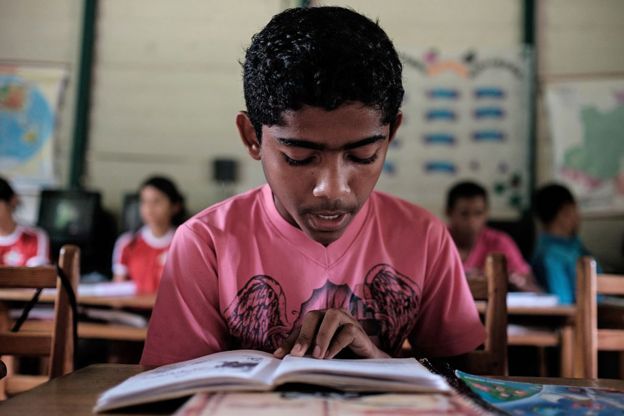 Un niño lee un libro en un salón de clases.