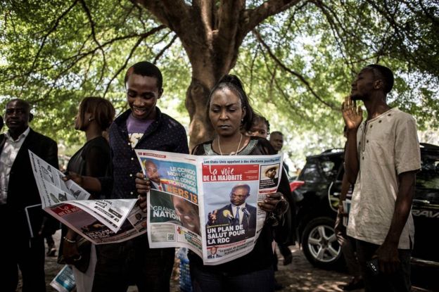 Supporters of the official DRCongo Presidential candidate, Emmanuel Ramazani Shadary, read a newspaper outside the Cathedral Notre-Dame Du Congo in Kinshasa on November 24, 2018, during the launch of his official electoral campaign.