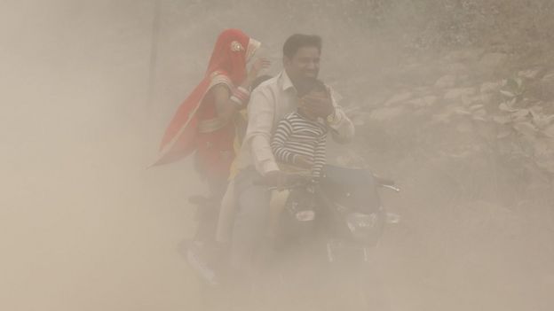 Pai, mãe e filhos em moto em meio a nuvem de poeira