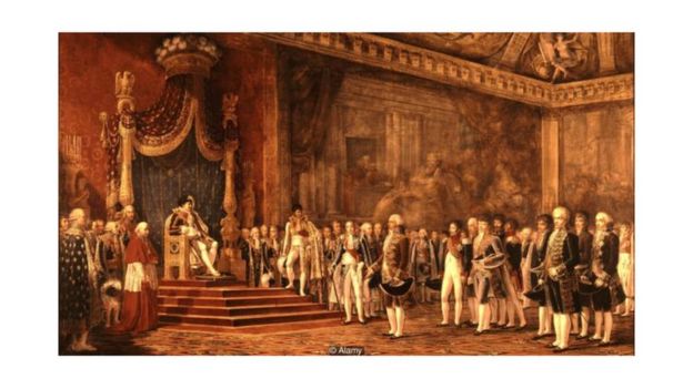 Esta pintura de Napoleão no Palácio de Versalhes, em 1809, mostra o imperador francês sentado enquanto todos ao lado permanecem em pé