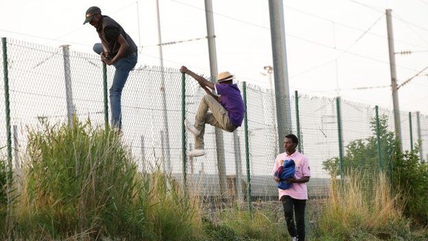 Migrants climb over a fence in Coquelles near Calais